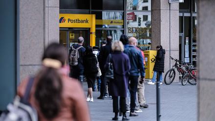 Kunden stehen in einer Warteschlange vor einer Filiale einer Postbank.