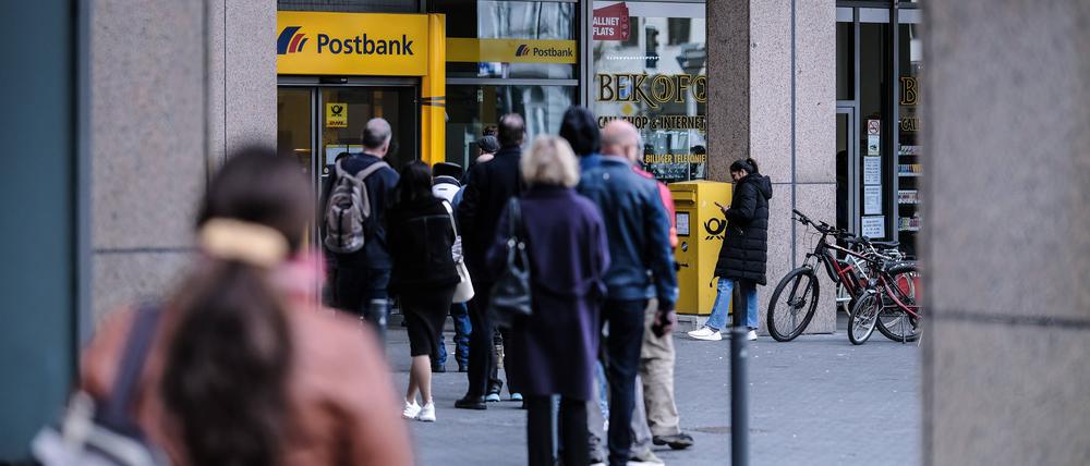 Kunden stehen in einer Warteschlange vor einer Filiale einer Postbank.
