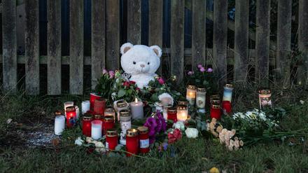 30.09.2023, Hessen, Bad Emstal: Kerzen, Blumen und ein großer Plüschteddy sind vor einem Zaun am Fundort zu sehen.