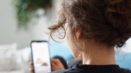 Eine Frau liegt auf einem Sofa und schaut sich ein Video auf der Social-Media-Plattform Instagram auf ihrem Handy an.