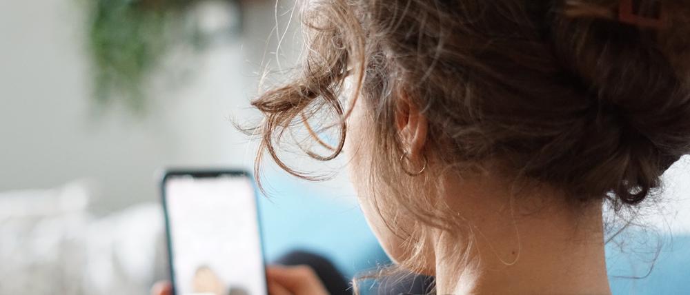 Eine Frau liegt auf einem Sofa und schaut sich ein Video auf der Social-Media-Plattform Instagram auf ihrem Handy an.