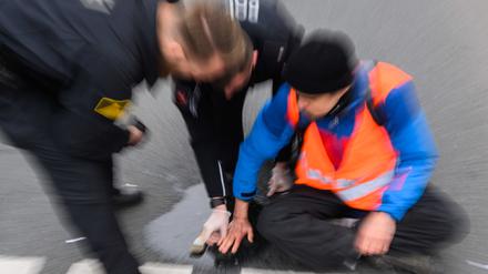 ARCHIV - 20.02.2023, Niedersachsen, Hannover: Polizisten versuchen festgeklebte Hände von Aktivisten der Gruppierung «Letzte Generation» am Deisterkreisel in Hannover mit Speiseöl von der Straße abzulösen. Auch In Berlin kam es am Dienstagabend zu Aktionen der Aktivisten.  (zu dpa: «Champions League: Klima-Aktivisten verzögern Anreise für Union-Fans») Foto: Julian Stratenschulte/dpa +++ dpa-Bildfunk +++
