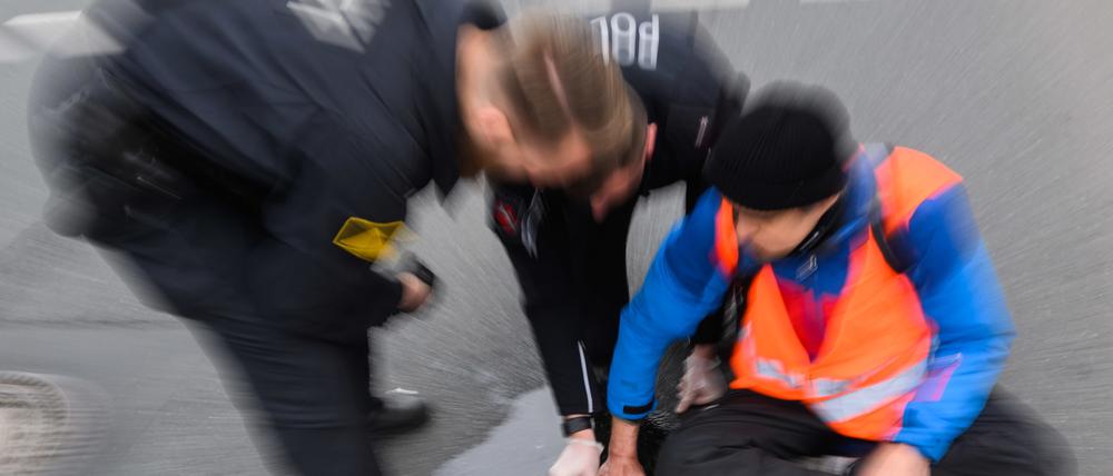 ARCHIV - 20.02.2023, Niedersachsen, Hannover: Polizisten versuchen festgeklebte Hände von Aktivisten der Gruppierung «Letzte Generation» am Deisterkreisel in Hannover mit Speiseöl von der Straße abzulösen. Auch In Berlin kam es am Dienstagabend zu Aktionen der Aktivisten. (zu dpa: «Champions League: Klima-Aktivisten verzögern Anreise für Union-Fans») Foto: Julian Stratenschulte/dpa +++ dpa-Bildfunk +++