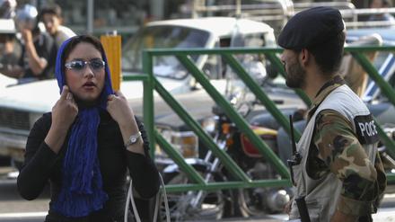 Eine Frau im Iran rückt sich vor einem Sicherheitsmann das Kopftuch zurecht.