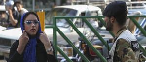 Eine Frau im Iran rückt sich vor einem Sicherheitsmann das Kopftuch zurecht.