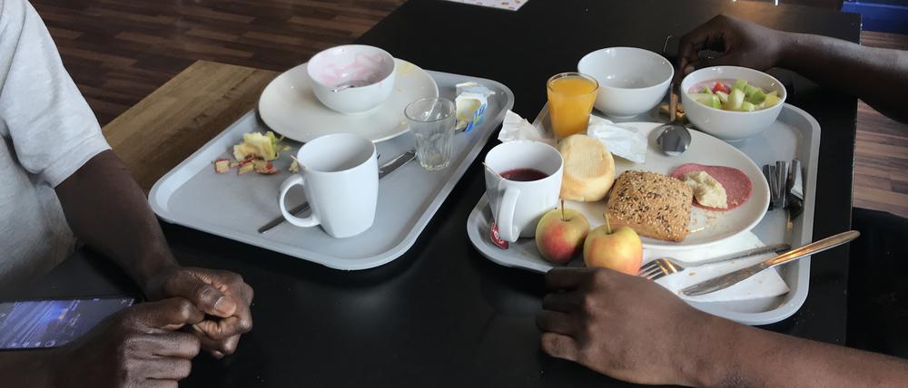 Ein geflüchteter Nigerianer und ein Tourist aus Budapest frühstücken in einem Hostel im Prenzlauer Berg. Sie haben sich an der Essensausgabe kennengelernt.