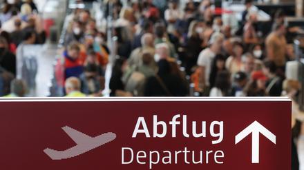 Am Flughafen Berlin-Brandenburg stehen zahlreiche Reisende in einer Schlange zur Sicherheitskontrolle hinter einem Schild mit der Aufschrift „Abflug“.