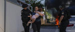 Israelische Polizei evakuiert eine Frau und ein Kind von einem Ort, der von einer aus dem Gazastreifen abgefeuerten Rakete getroffen wurde. An anderen Orten wurden auch Kinder und Babys getötet.