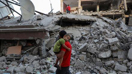 Ein Mann geht mit einem Kind auf dem Arm an einem durch israelische Luftangriffe zerstörten Gebäude in der Stadt Chan Junis im südlichen Gazastreifen vorbei.