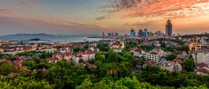 Qingdao, 1898 als Tsingtau an der Nordost-Küste Chinas während des Kolonialismus von Deutschen gegründet. Heute erinnern noch immer daran die roten Dächer der historischen Häuser vor der Skyline der modernen Millionenstadt. 