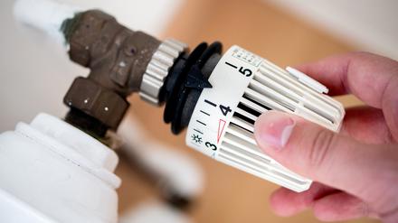 Ein Mann dreht in einer Wohnung am Thermostat einer Heizung. 