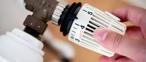 Ein Mann dreht in einer Wohnung am Thermostat einer Heizung.