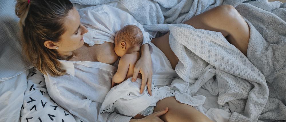 Eine Mutter liegt im Bett und stillt ihr Kind