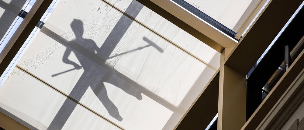 Schatten eines Arbeiters, der ein Glasdach reinigt.