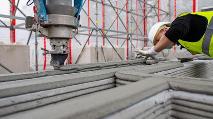 Ein Mitarbeiter eines Bauunternehmens beobachtet einen 3D-Drucker, der die nächste Schicht Beton auf Wände aufträgt. (Archivfoto) 