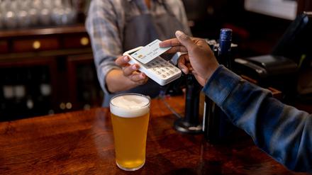 Close-up on a man making a contactless payment at the pub while drinking beer - financial technology concepts