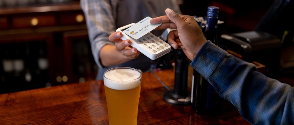 Close-up on a man making a contactless payment at the pub while drinking beer - financial technology concepts