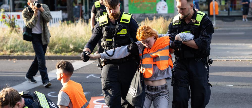 Eine Aktivistin wird von zwei Polizisten von der Straße getragen.