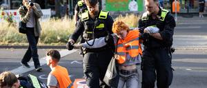 Eine Aktivistin wird von zwei Polizisten von der Straße getragen.