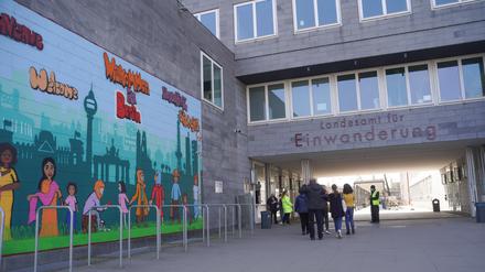 Menschen gehen am Landesamt für Einwanderung (LEA) am Friedrich-Krause-Ufer neben einem Wandbild entlang. 