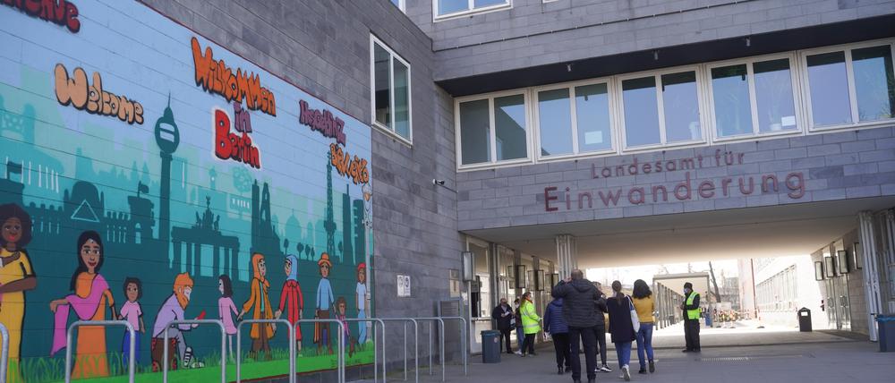 Menschen gehen am Landesamt für Einwanderung (LEA) am Friedrich-Krause-Ufer neben einem Wandbild entlang.
