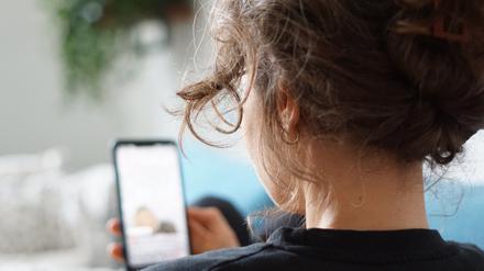 Eine Frau liegt auf einem Sofa und schaut auf ihr Handy (Symbolbild)