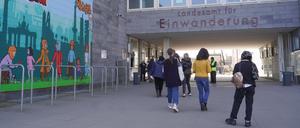 Menschen gehen am Landesamt für Einwanderung am Friedrich-Krause-Ufer neben einem Wandbild entlang.