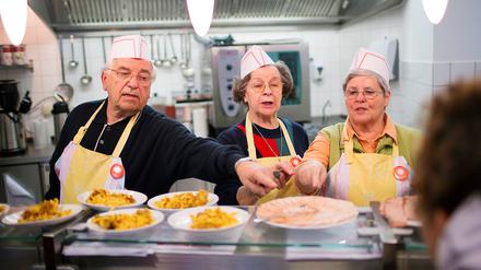 Ehrenamtliche Helfer teilen in der Caritas-Wärmestube am Bundesplatz in Berlin Essen aus. 