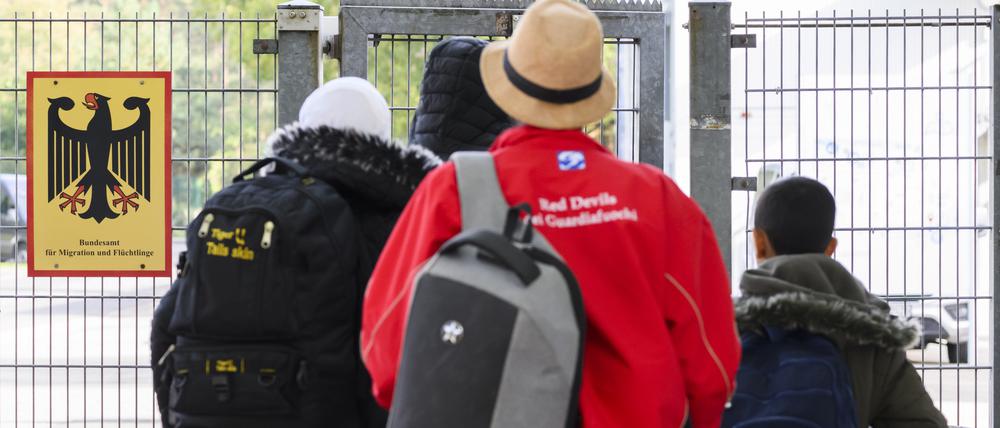 Geflüchtete betreten neben einem Schild vom Bundesamt für Migration und Flüchtlinge die Landesaufnahmebehörde Niedersachsen am Standort Braunschweig.