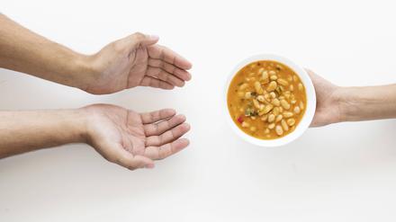 Hand gibt Suppenschüssel an bedürftige Person