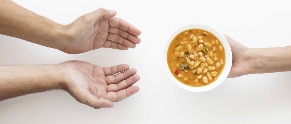 Hand gibt Suppenschüssel an bedürftige Person