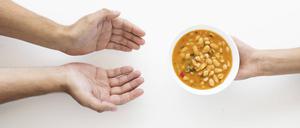 Hand gibt Suppenschüssel an bedürftige Person