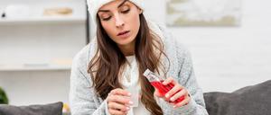 sick young woman in warm clothes pouring red cough syrup while sitting on couch at home