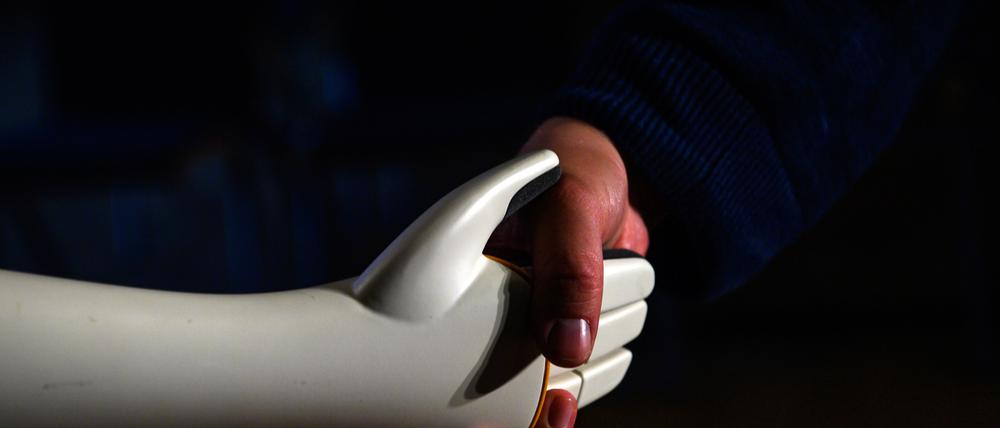 Eine menschliche Hand greift die Hand eines humanoiden Roboters.