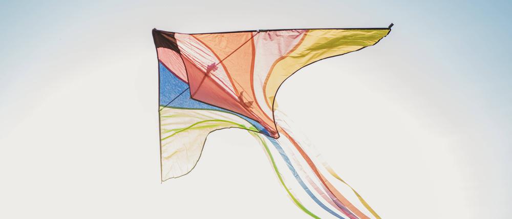 Ein bunter Drache fliegt am blauen Himmel.