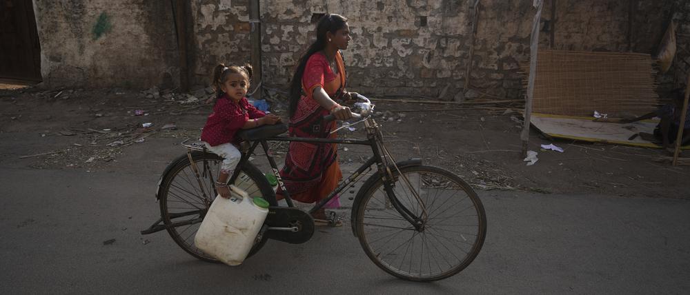 Eine Frau mit einem Kind transportiert Wasser mit einem Fahrrad aus einem öffentlichen Wasserhahn in einem Slumgebiet. In Südasien leiden weltweit am meisten Kinder an Wasserknappheit.