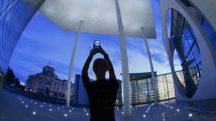Germany Berlin, Nov 01/2022. a female tourist at twilight photographing various German government building including The Reichstag parliament building seen on left of frame.using a smart phone, composite image.