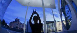 Germany Berlin, Nov 01/2022. a female tourist at twilight photographing various German government building including The Reichstag parliament building seen on left of frame.using a smart phone, composite image.