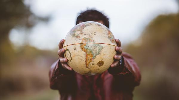 A closeup shot of a male wearing a leather jacket holding a globe in front of him with a blurred background
Verwendung nur online für "Themenspezial Bühne"