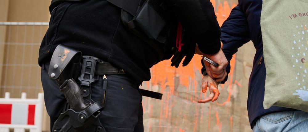 Ein Polizeibeamter (l) nimmt eine Klimaaktivistin in Gewahrsam, die das Brandenburger Tor mit oranger Farbe bemalt hat.