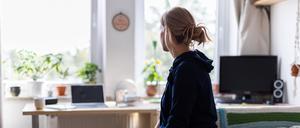 Eine Studentin sitzt auf dem Bett in ihrem WG-Zimmer und schaut aus dem Fenster (gestellte Szene). 