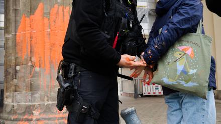 Ein Polizeibeamter nimmt eine Klimaaktivistin in Gewahrsam, die das Brandenburger Tor mit oranger Farbe bemalt hat.