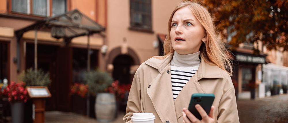 Eine Frau mit Smartphone reagiert genervt auf einen Anruf.