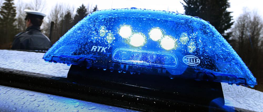 Ein Polizist steht im Regen vor einem Streifenwagen, dessen Blaulicht aktiviert ist.