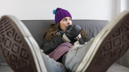 Eine Frau sitzt auf dem Sofa, mit Handschuhen und Pudelmütze.