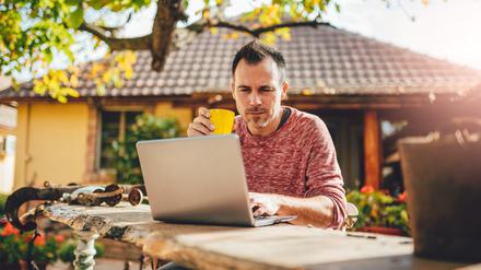 Men sitting in the at backyard patio drinking coffee and using laptop
Workation