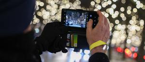 Eine Person fotografiert den Start der Weihnachtsbeleuchtung am Ku’damm an der Grünfeld-Ecke. Mangels Finanzen ist sie weniger opulent als in anderen Jahren.