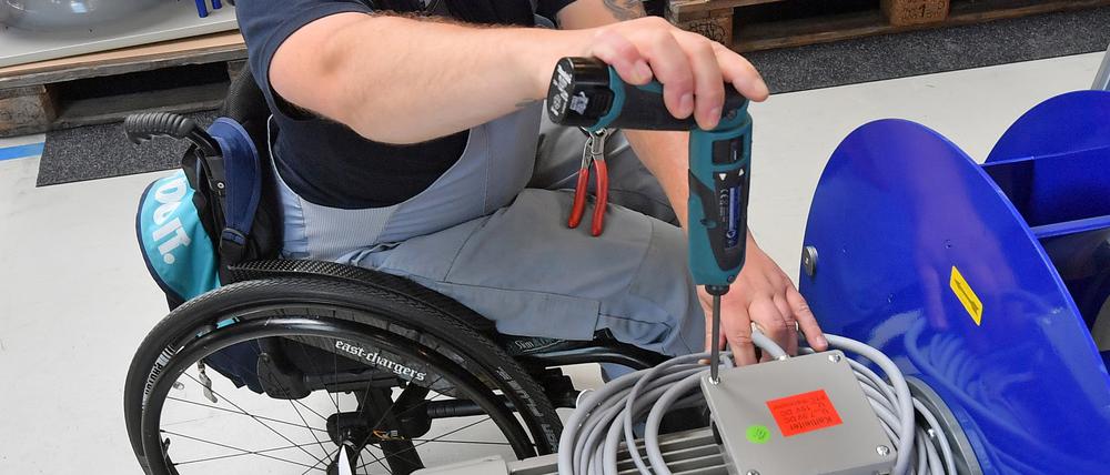 An einem Arbeitsplatz für Motorklemmen ist ein Mitarbeiter im Rollstuhl mit Montagearbeiten beschäftigt.