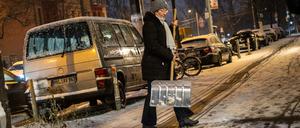 Frau beseitigt mit einem Schneeschieber den frisch gefallenen Schnee auf dem Gehweg auf der Eberswalder Straße in Berlin.