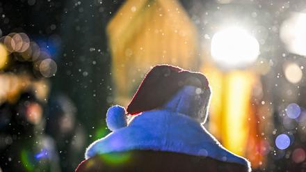 Ein Weihnachtsmann geht niedergeschlagen auf dem Weihnachtsmarkt vor dem Roten Rathaus bei leichtem Schneefall.